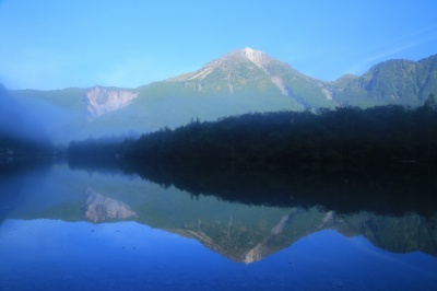 朝霧立ち込める大正池の水鏡に映る穂高岳、幻想的な上高地の絶景写真。シンメトリー構図。